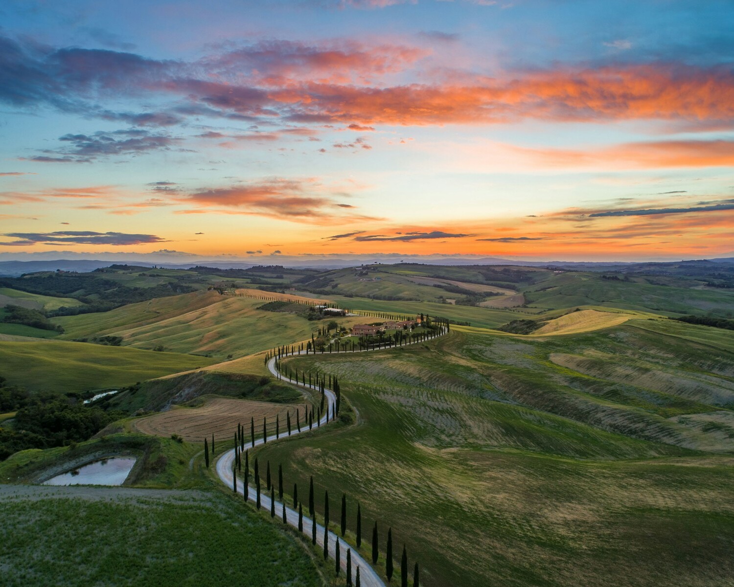 road between green grass field near mountains under blue and brown sky at golden hour